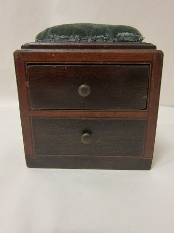 Gerät für die Handarbeit, antik 
Wie eine Kommode geformt, - aus Holz
Mit einer Schraube damit dass es möglich ist, das Gerät auf den Tisch 
festzuspannen
Kommode mit einer Schublade
Um 1830
H: 14cm, L: 12,5cm, D: 8,5cm
Bemerken Sie bitte: Finerschad