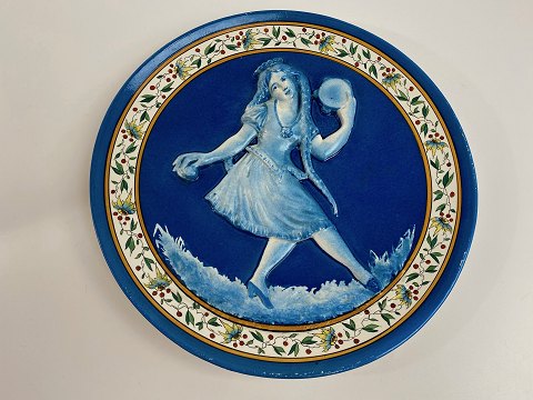 Französische Fayence Platte mit Motiv des blauen Mädchens mit langen Zöpfen im 
Relief. Das Mädchen tanzt und spielt Musik mit Kastagnetten und Tamburin - 
ersten Hälfte des 20. Jahrhunderts